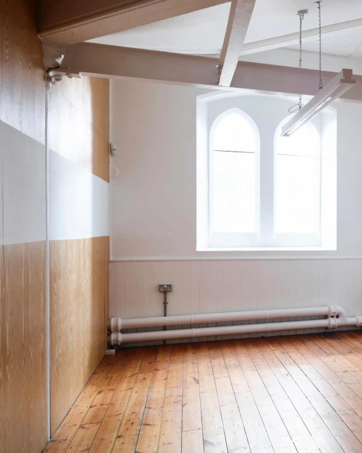 Empty room featuring wood floor, white walls, and two arched windows, complemented by a radiator and minimal furnishings, spacious design.