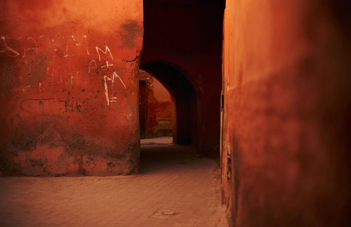 An atmospheric view down a narrow alleyway with arched openings and textured orange walls featuring painted white graffiti.