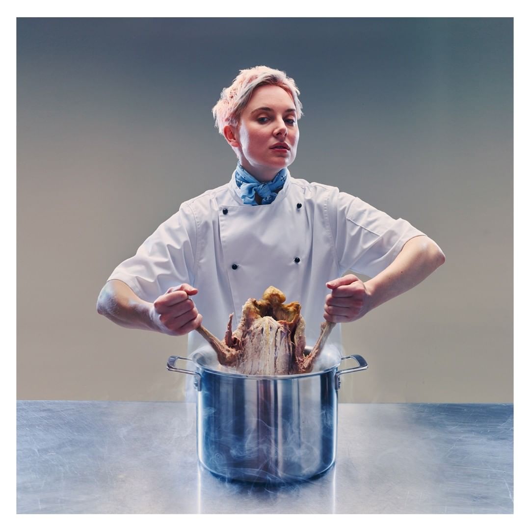 A culinary professional in a white chef's coat holds a metallic pot with a cooked turkey, steam rising, set against a gradient backdrop.