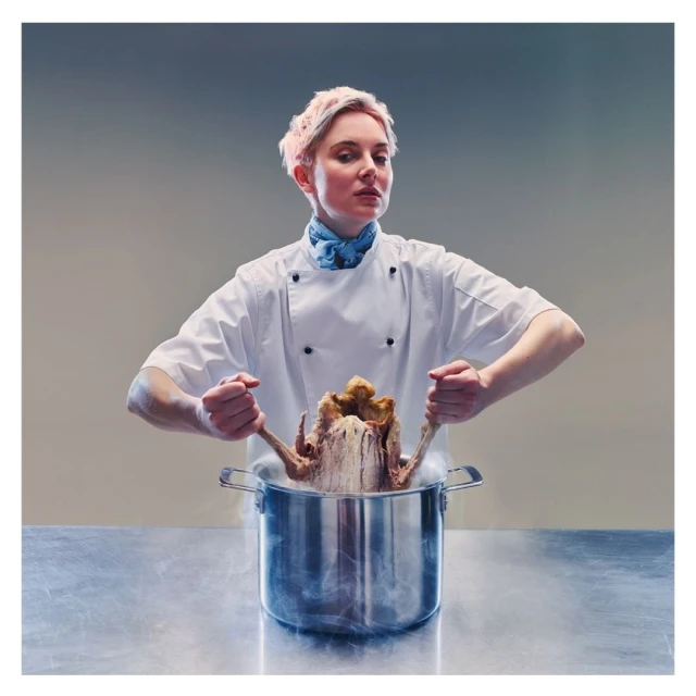 A culinary professional in a white chef's coat holds a metallic pot with a cooked turkey, steam rising, set against a gradient backdrop.