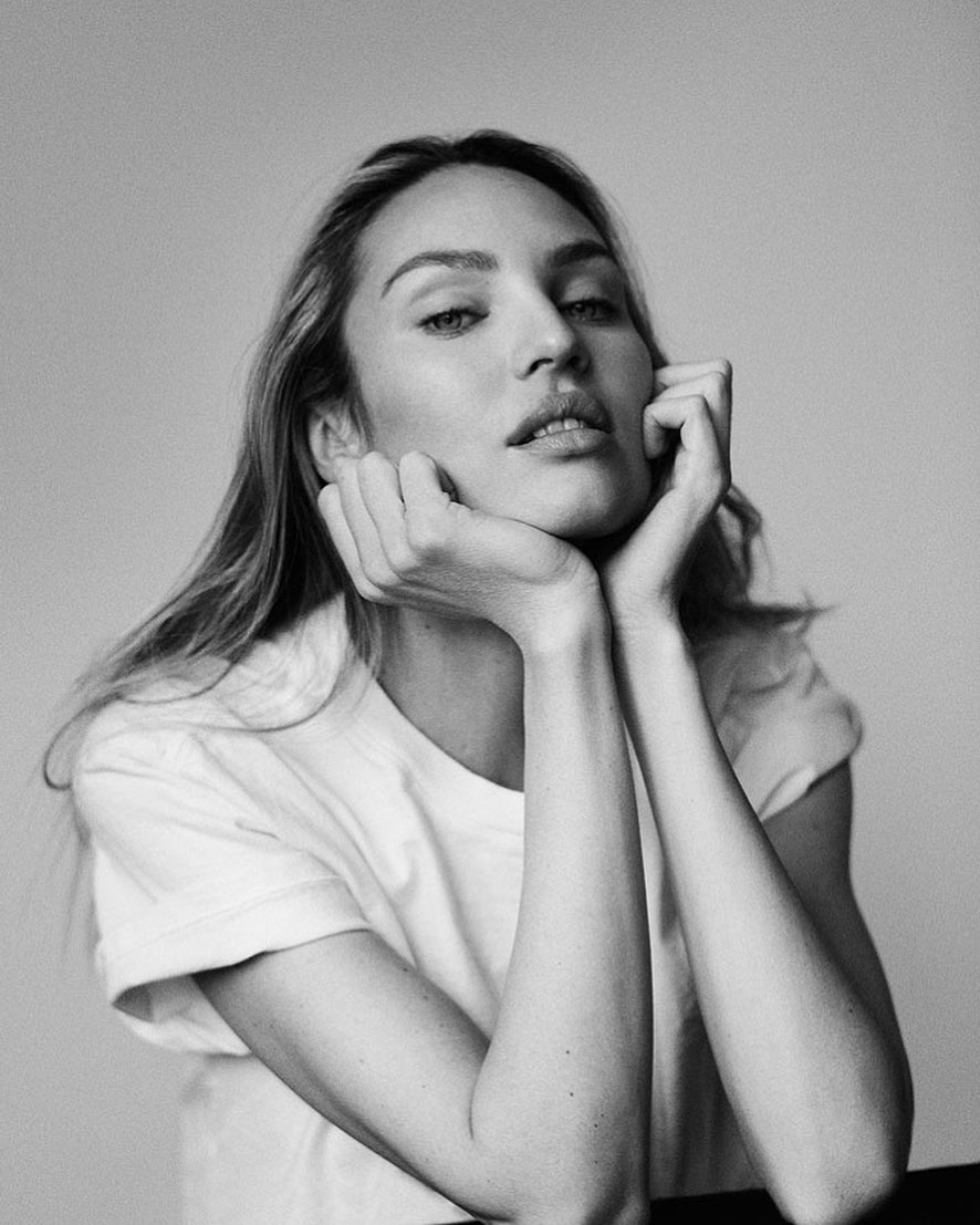 Black and white portrait of a young woman with long hair, wearing a t-shirt, resting her face on her hands in a relaxed pose.