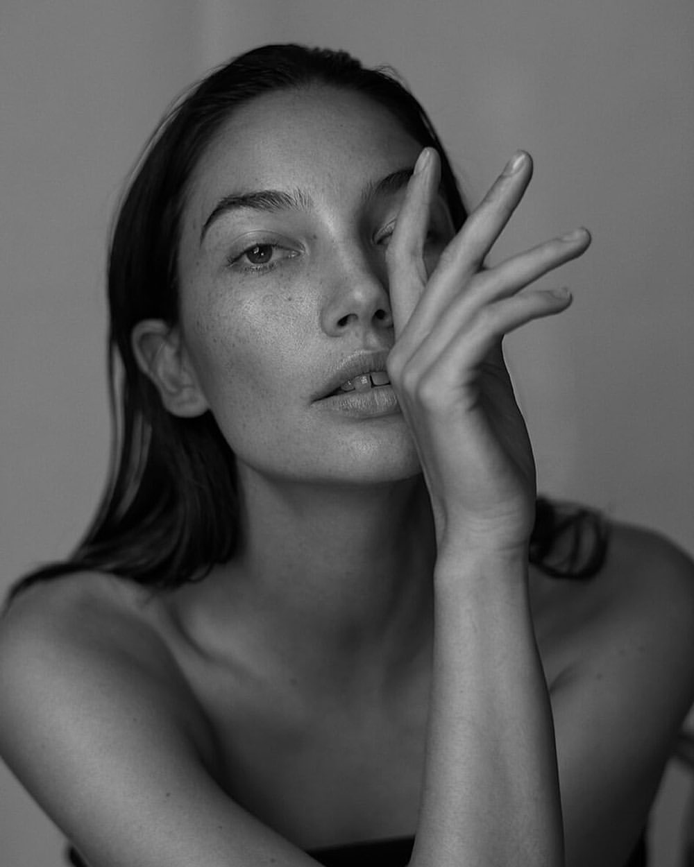 Black-and-white portrait of a fair-skinned adult woman with dark hair. She is covering part of her face with her hand.
