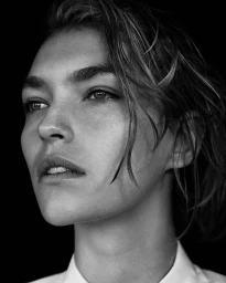 Close-up black and white portrait of a woman with wet hair and a white collar against a dark background.