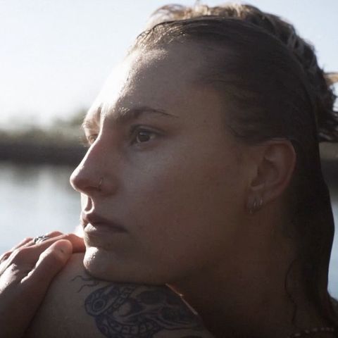 Profile portrait of a woman resting her chin on a tattooed arm outdoors near water by Alexa Singer