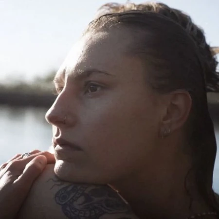 Profile portrait of a woman resting her chin on a tattooed arm outdoors near water by Alexa Singer
