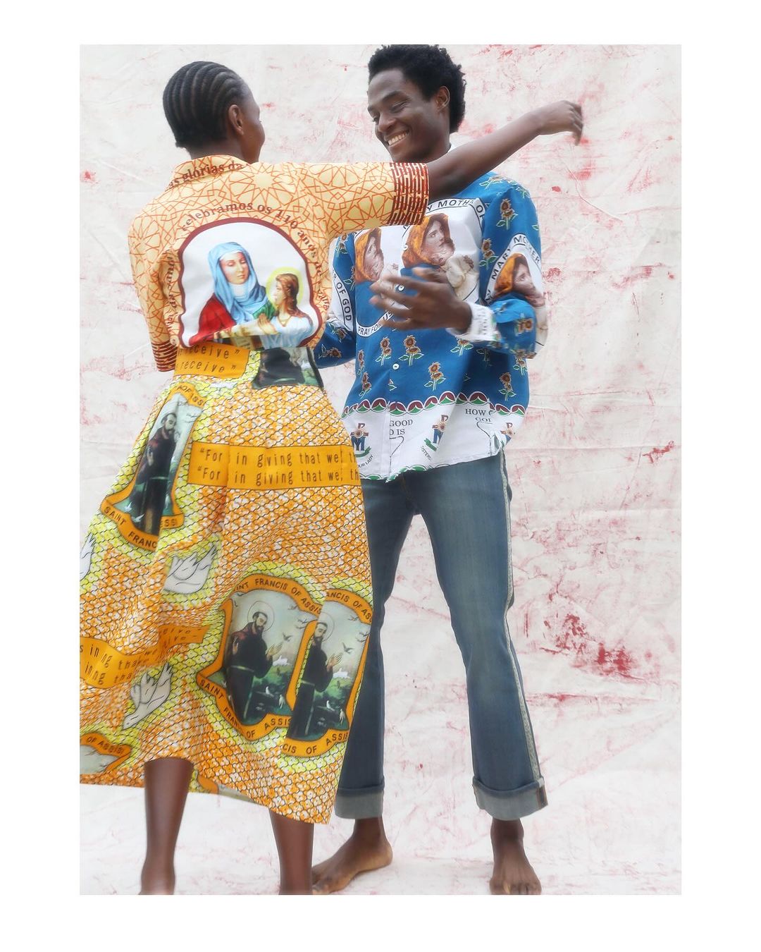 A cheerful couple poses in printed apparel. The man is in blue jeans, while the woman wears a dress and top with a yellow-orange print.