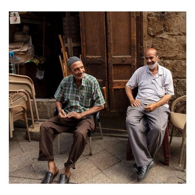 Two elderly men seated on chairs outside a building, one wearing a mask, creating a candid, casual scene with textured details.