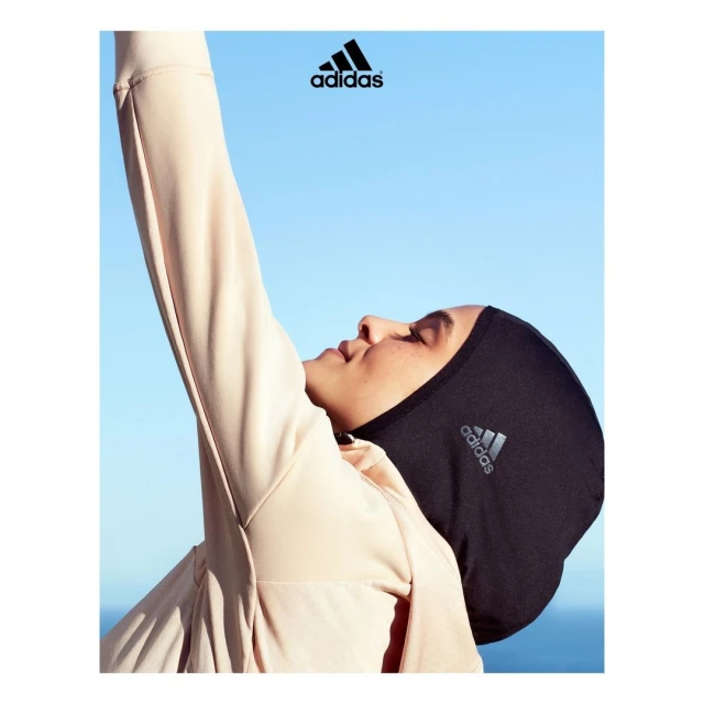Woman wearing Adidas head covering and sporty top against a clear blue sky, posing with arm raised, Adidas logo prominently displayed.