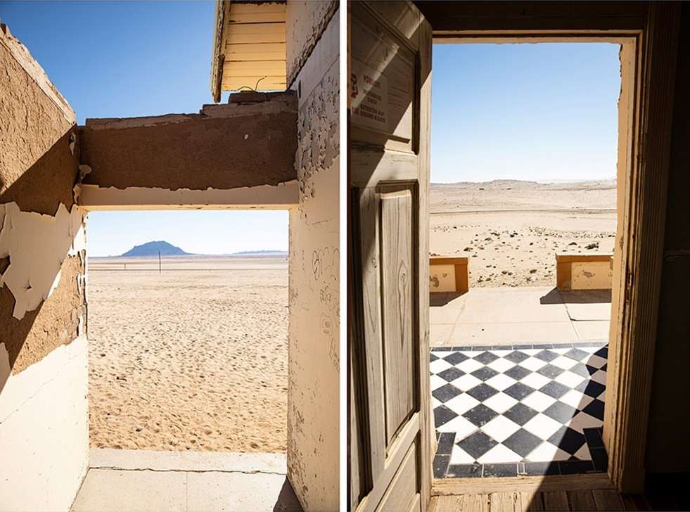 Two abandoned buildings in a desert landscape, viewed through doorways. Clear blue sky above the sandy terrain and distant mountains.