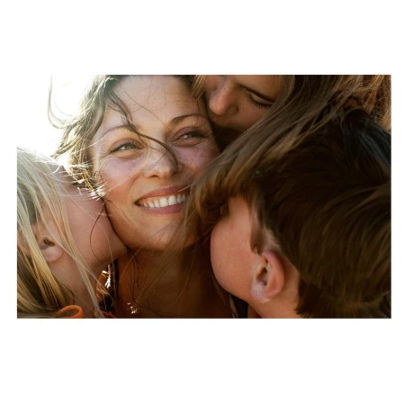 Close-up portrait of a smiling woman surrounded by children embracing her in warm sunlight.