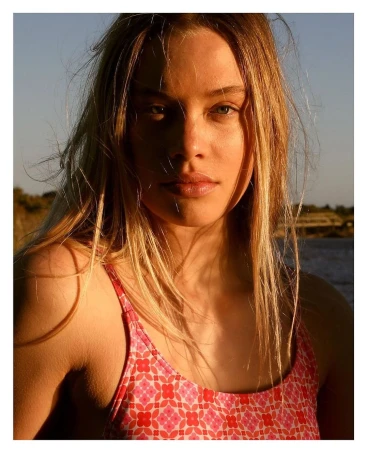 Close-up portrait of a blonde woman wearing a pink patterned swimsuit outdoors during golden hour sunlight.