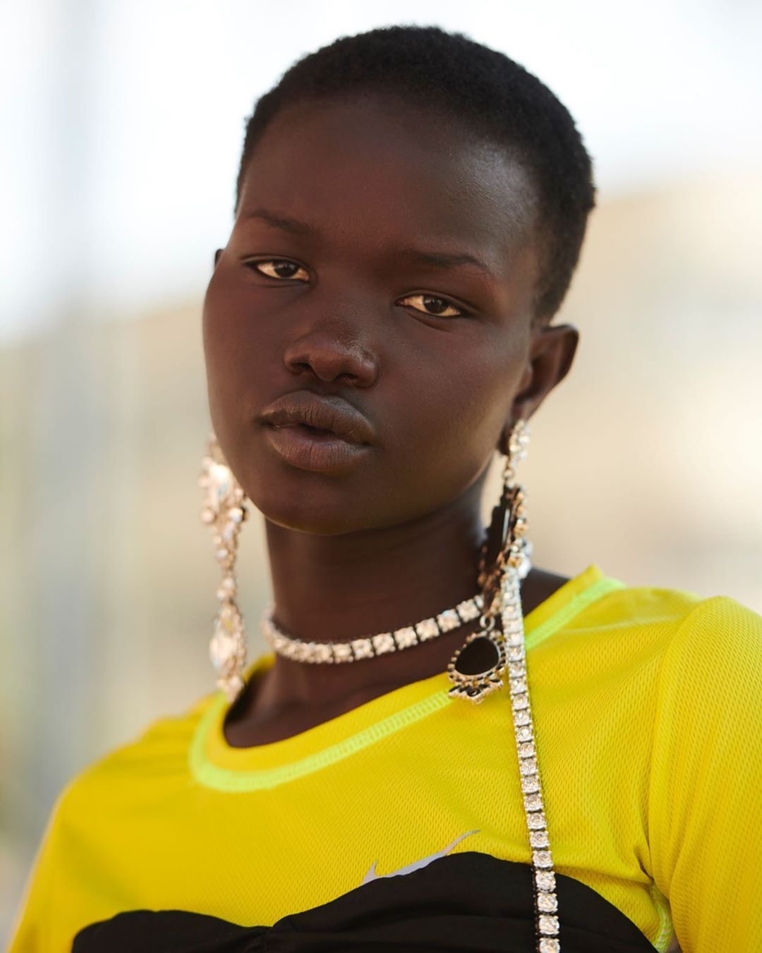 Close-up of an African-descent adult female model with short hair wearing a yellow-and-black top and jewelry, shot indoors.