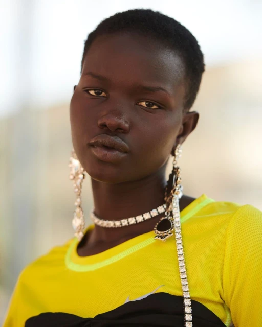 Close-up of an African-descent adult female model with short hair wearing a yellow-and-black top and jewelry, shot indoors.