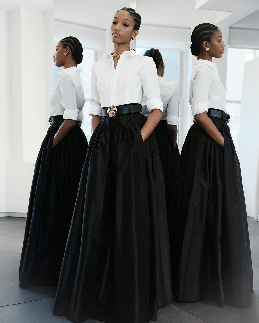 Model with braided hair wearing a white button-down shirt and long black skirt reflected in multiple mirrors