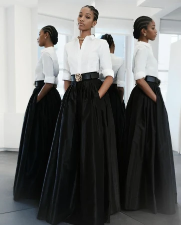 Model with braided hair wearing a white button-down shirt and long black skirt reflected in multiple mirrors