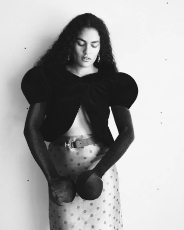 Monochrome fashion portrait of a model with long curly hair wearing a dark puffed-sleeve top and polka-dot skirt.