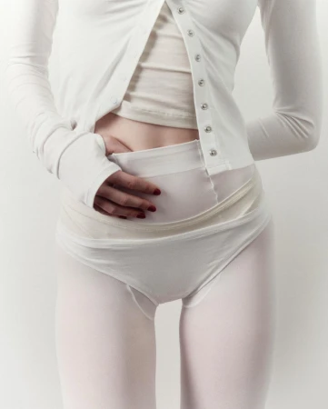 Torso shot of an adult female wearing a white buttoned cardigan, top, and matching underwear on a white backdrop in a photo studio.
