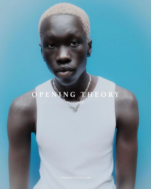 Portrait of a young adult with bleached blonde hair and silver chain against a bright blue background in a minimalist fashion shot.