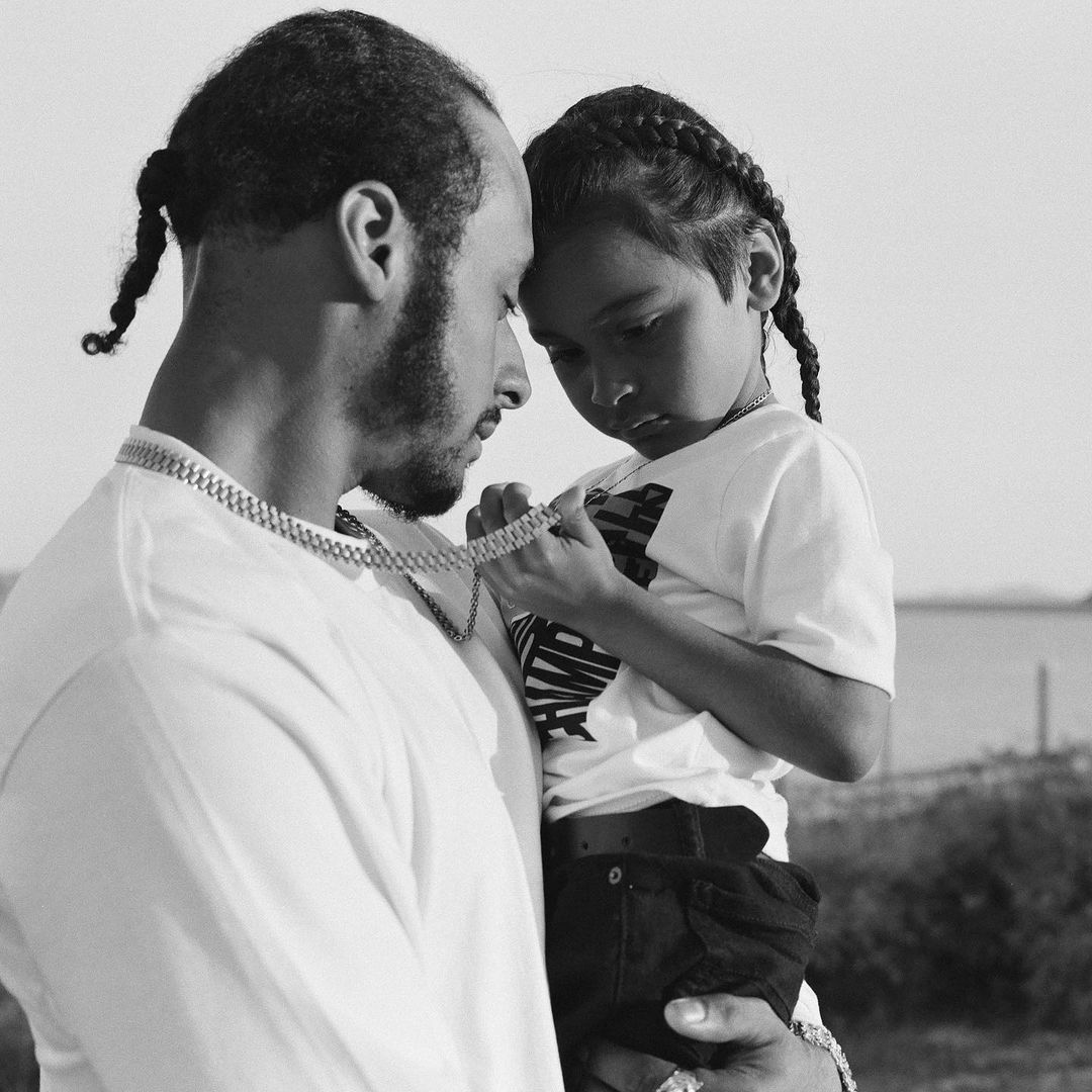 A black and white image captures a man cradling a young boy, their heads close together in a tender moment. The light highlights their faces.