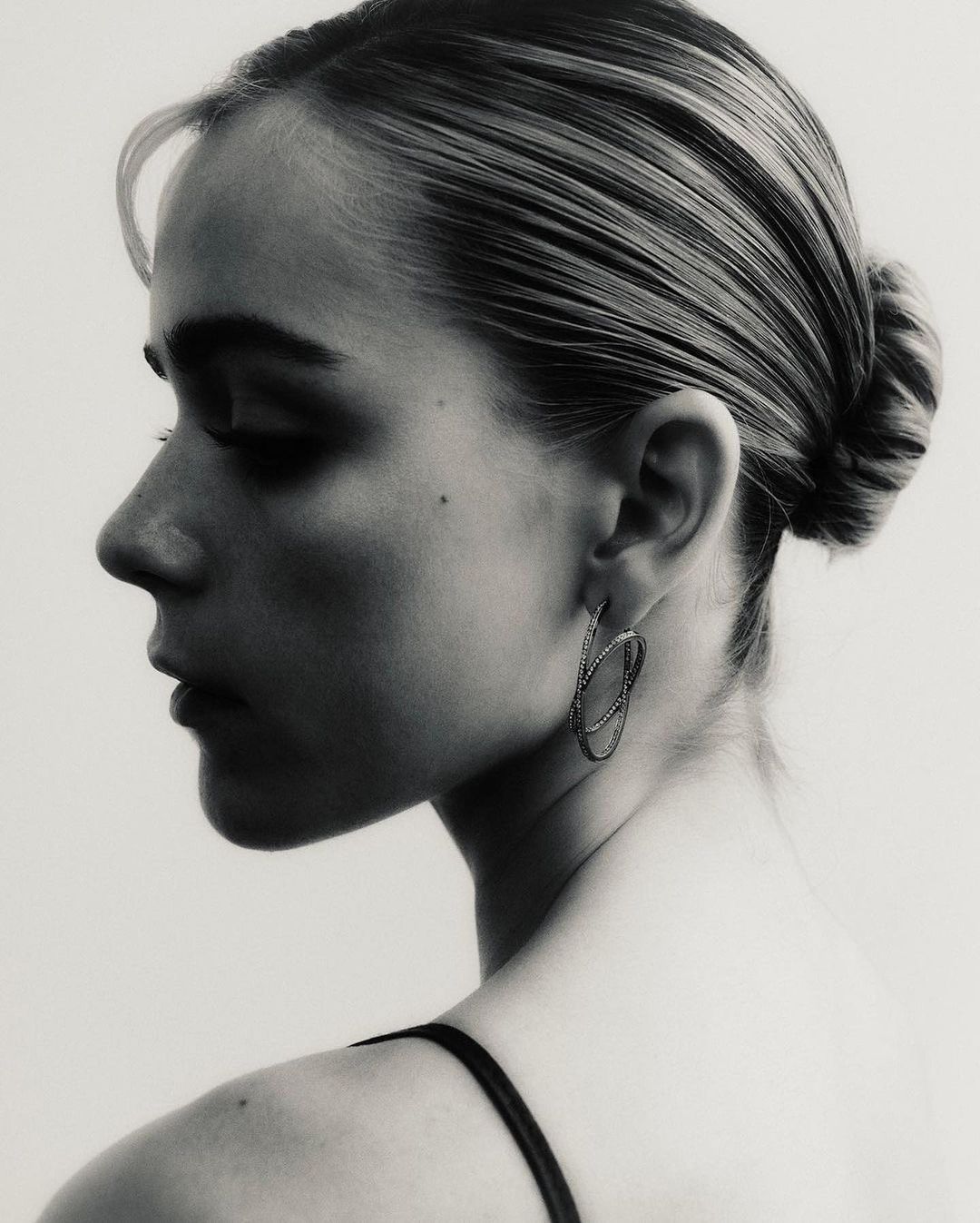 Monochrome portrait of a fair-skinned woman looking over her shoulder wearing sculptural earrings in a minimalist studio setting.