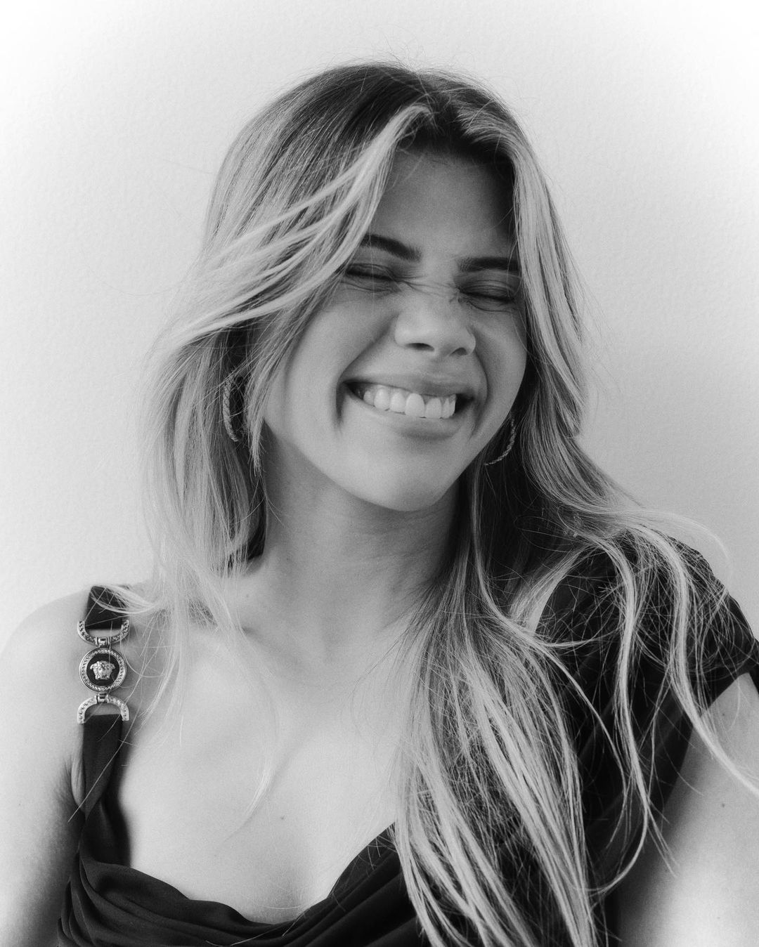 Close-up portrait of a smiling woman with long blonde hair laughing with closed eyes against a plain background