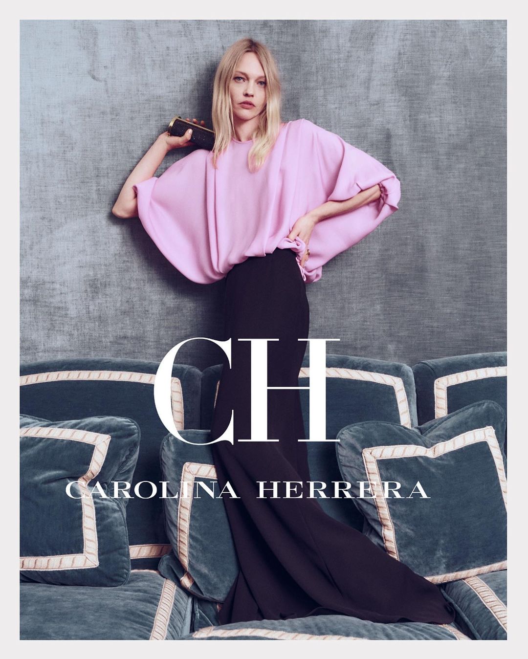 A fashion shot features a blonde female model wearing a pink top and black skirt, holding a clutch, posing on a blue tufted couch with brand text.