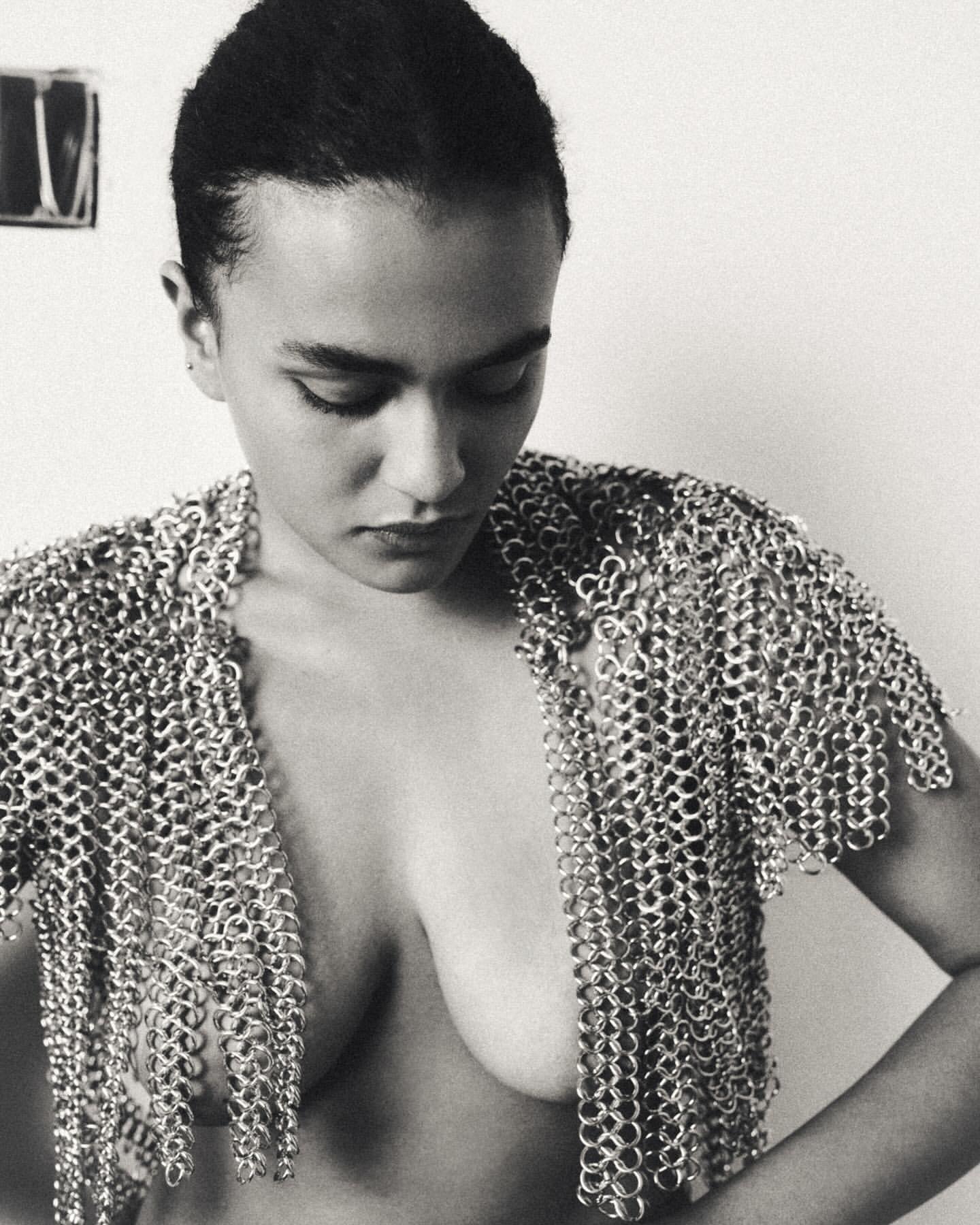 Monochrome portrait of a woman wearing metal chainmail, shot in a photo studio with a plain backdrop and diffused, even lighting.