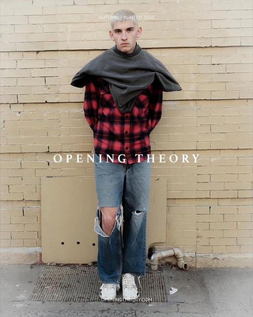 Fashion shot of a male model in tattered jeans, plaid shirt, and grey top, posing against a brick wall for Opening Theory Autumn/Winter 2023.