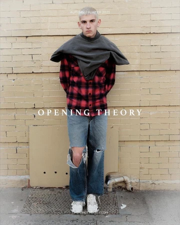 Fashion shot of a male model in tattered jeans, plaid shirt, and grey top, posing against a brick wall for Opening Theory Autumn/Winter 2023.