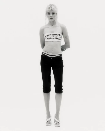Full-length shot of a slender woman in black capri pants and a white top, posing against a bright white background in a studio.