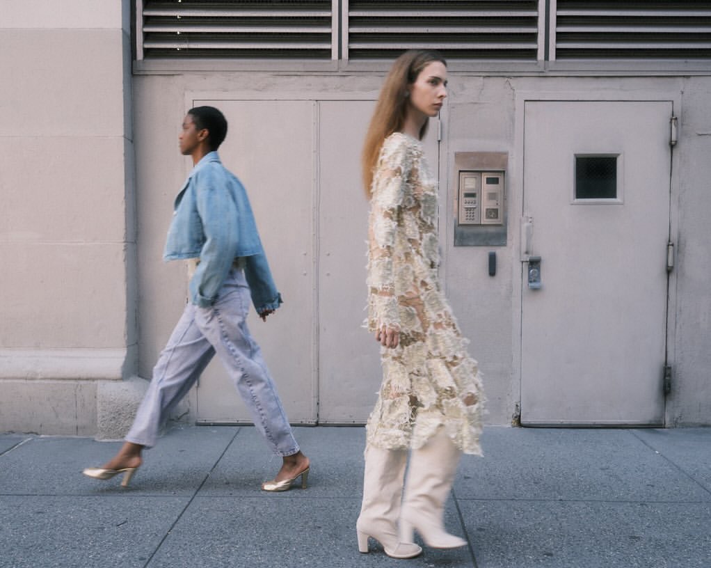 Two women in fashionable outfits walking on a sidewalk in an urban setting, showcasing contemporary street style.