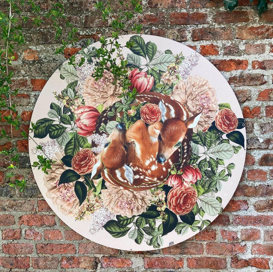 Whimsical illustration featuring a group of deer nestled among roses and other flowers in a roundel against a brick wall backdrop.