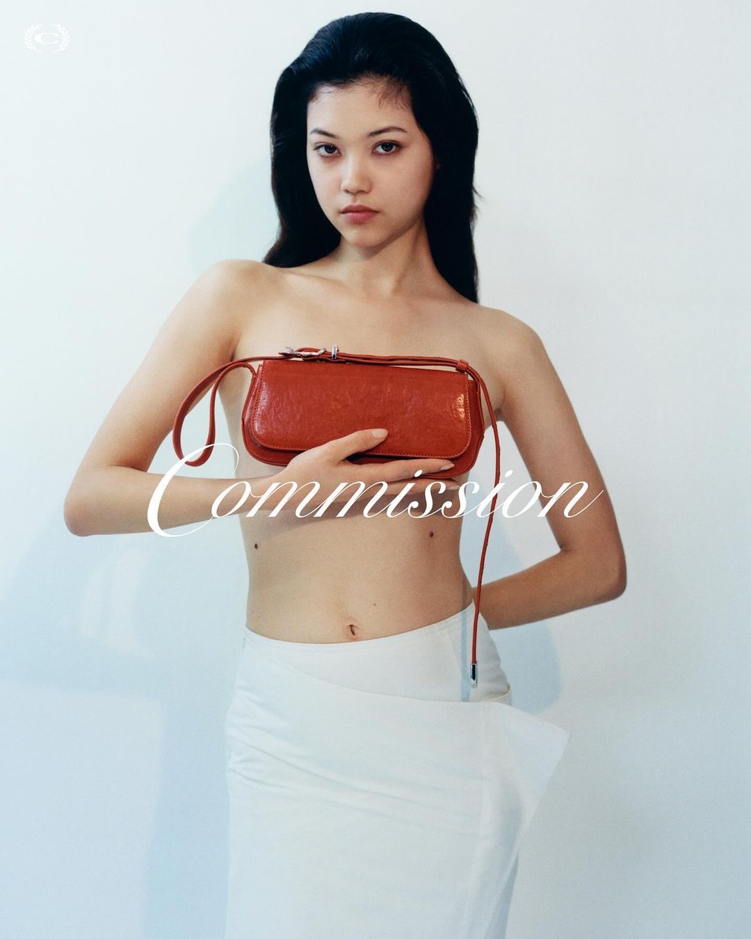 Portrait of an Asian woman holding a red purse, wearing a white skirt in front of a white wall for a fashion editorial photoshoot.