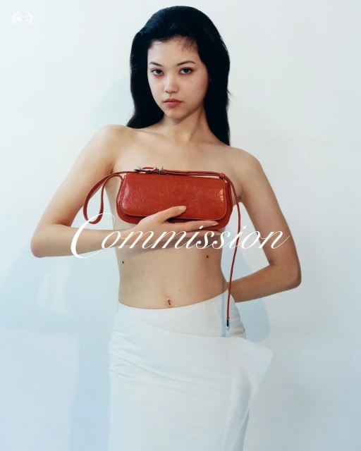 Portrait of an Asian woman holding a red purse, wearing a white skirt in front of a white wall for a fashion editorial photoshoot.
