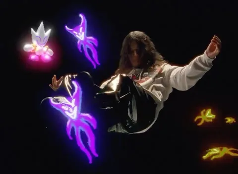 Woman in a sweatshirt poses in a surreal digital composition featuring glowing cartoon creatures on a dark background in a studio setting.