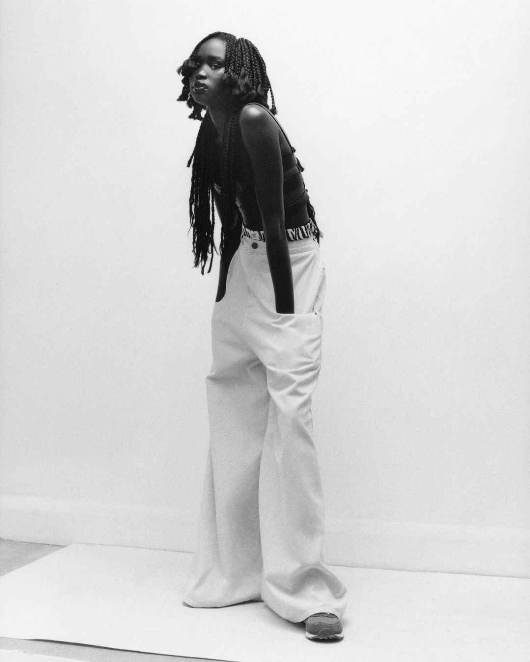 Portrait of a woman in wide-legged pants and a black top posing in a photo studio with a minimalist backdrop and neutral color palette.