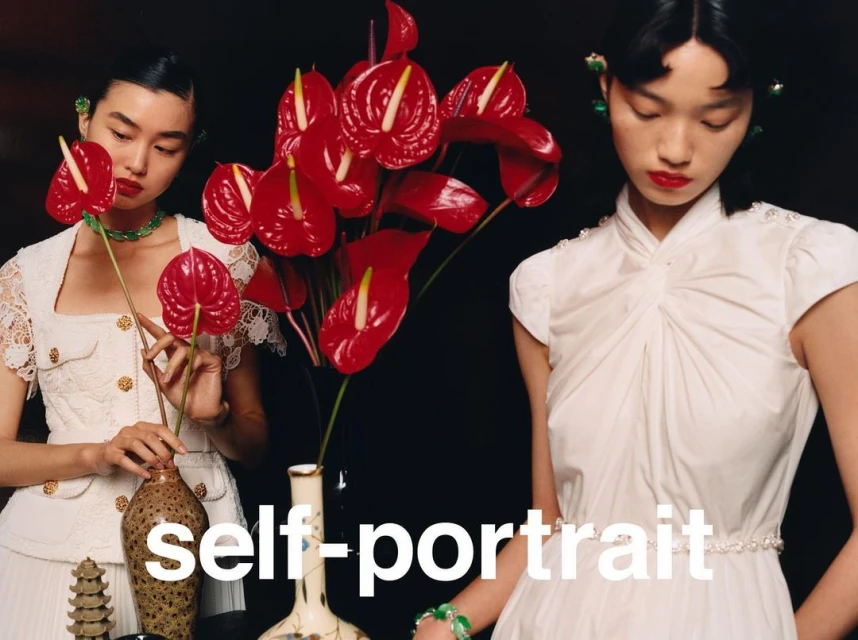 Two Asian women in white dresses pose with red Anthurium flowers and ceramic vases against a dark backdrop in a studio setting.