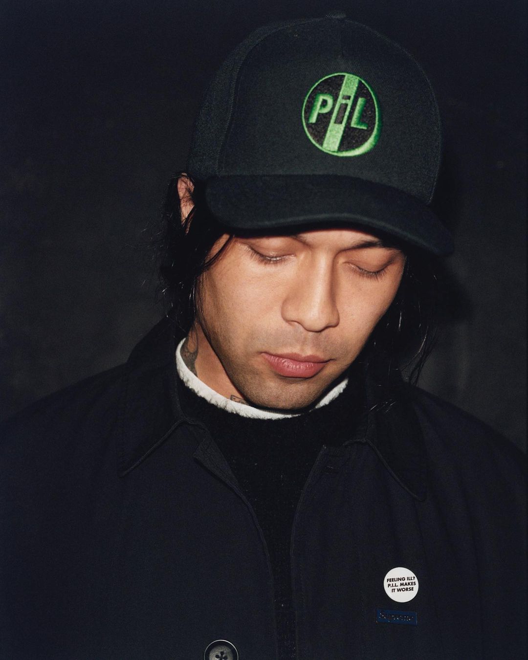 Portrait of a man wearing a black cap with a green PIL logo and a dark jacket, photographed by Alexandra Leese.