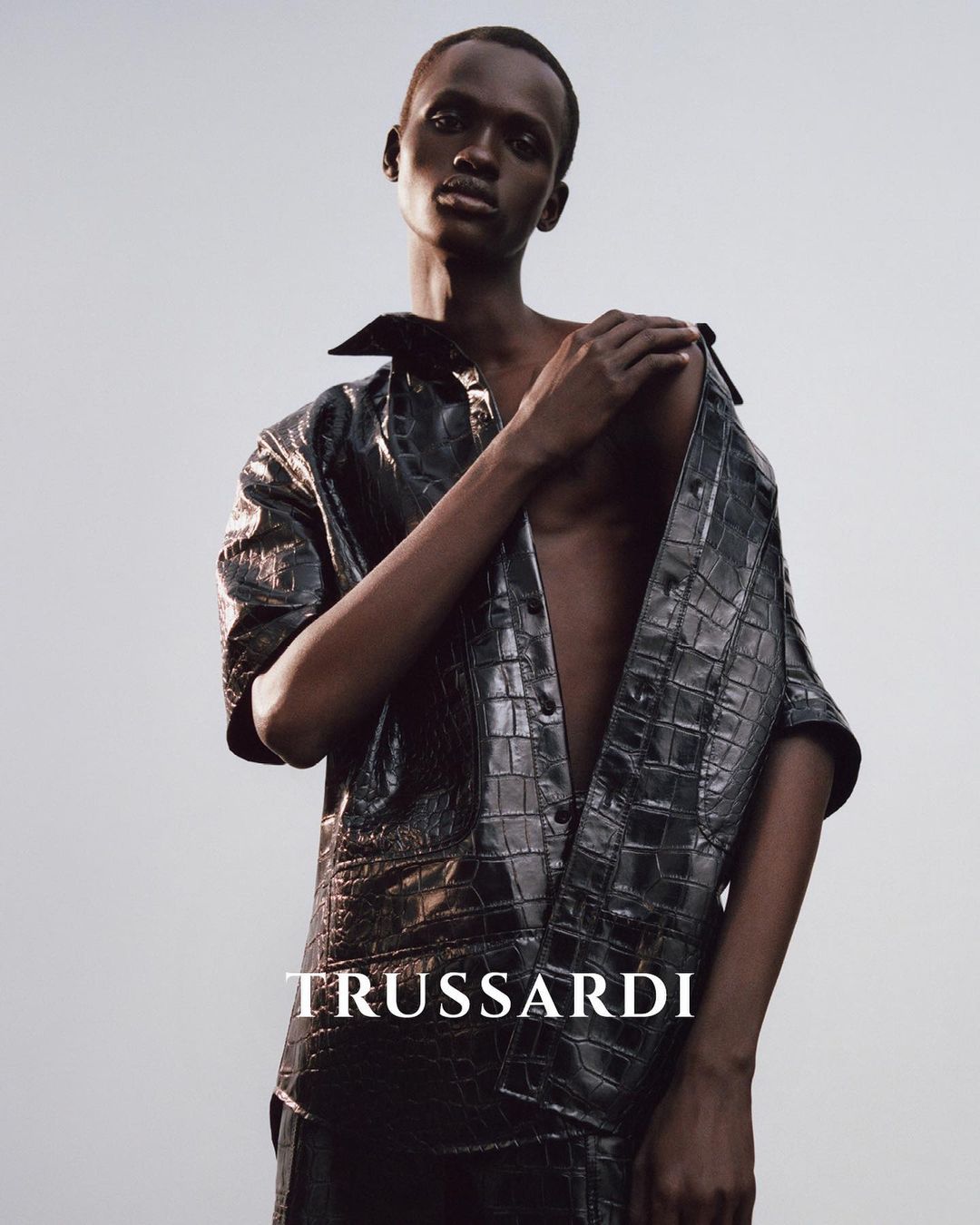Fashion editorial shot of an African American male model wearing a crocodile-patterned shirt, posing against a gradient background.
