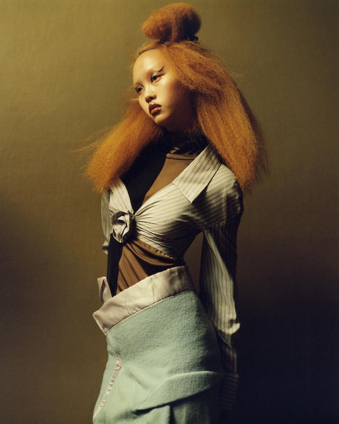 Striking fashion portrait of a stylish woman with red hair and a bold makeup look, posing in an elegantly designed blouse and skirt.