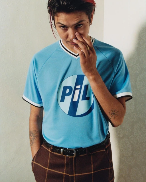 Portrait of a young adult male with dark hair and a blue t-shirt, indoors against a neutral wall, looking into the camera.