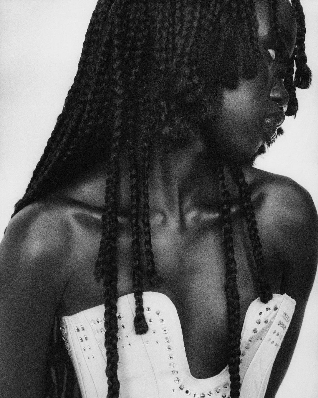 Close-up black and white shot of an African-American woman in a studded corset, with long braids, in a photo studio with diffused lighting.