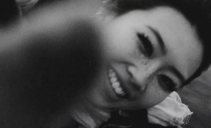 Black and white close-up of an adult female smiling, captured in a tilted eye-level shot with shallow depth of field.