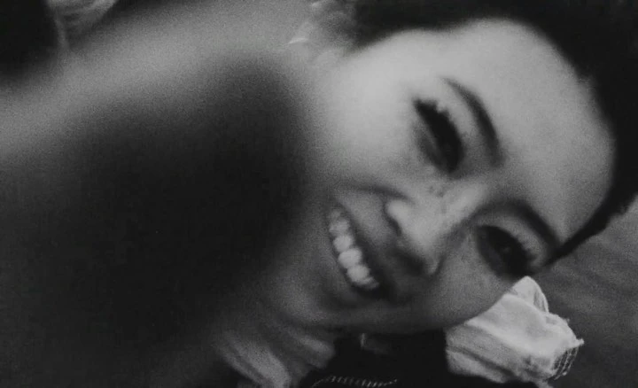 Black and white close-up of an adult female smiling, captured in a tilted eye-level shot with shallow depth of field.