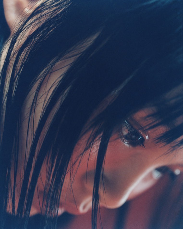 Close-up portrait of a young woman with long, dark hair and subtle makeup, captured in soft, diffused lighting.