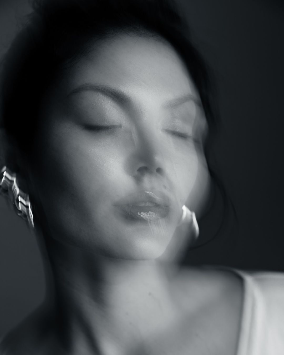 Close-up portrait of an adult woman with closed eyes, wearing earrings. The image has a blurred, dreamy quality in monochrome.