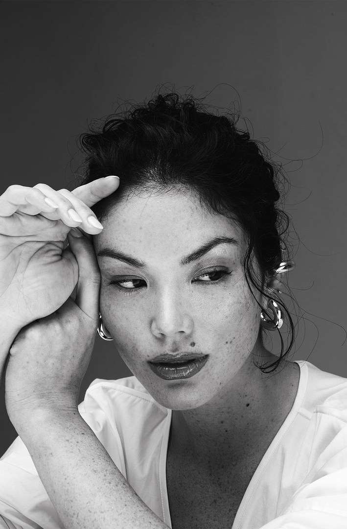 Black and white portrait of an adult female with dark hair, wearing hoop earrings, looking off to the side with her hand near her face.