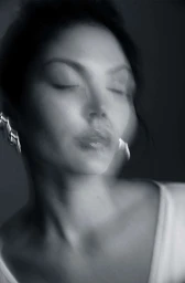Close-up monochrome portrait of a woman with eyes closed and motion blur effect, wearing a statement earring.