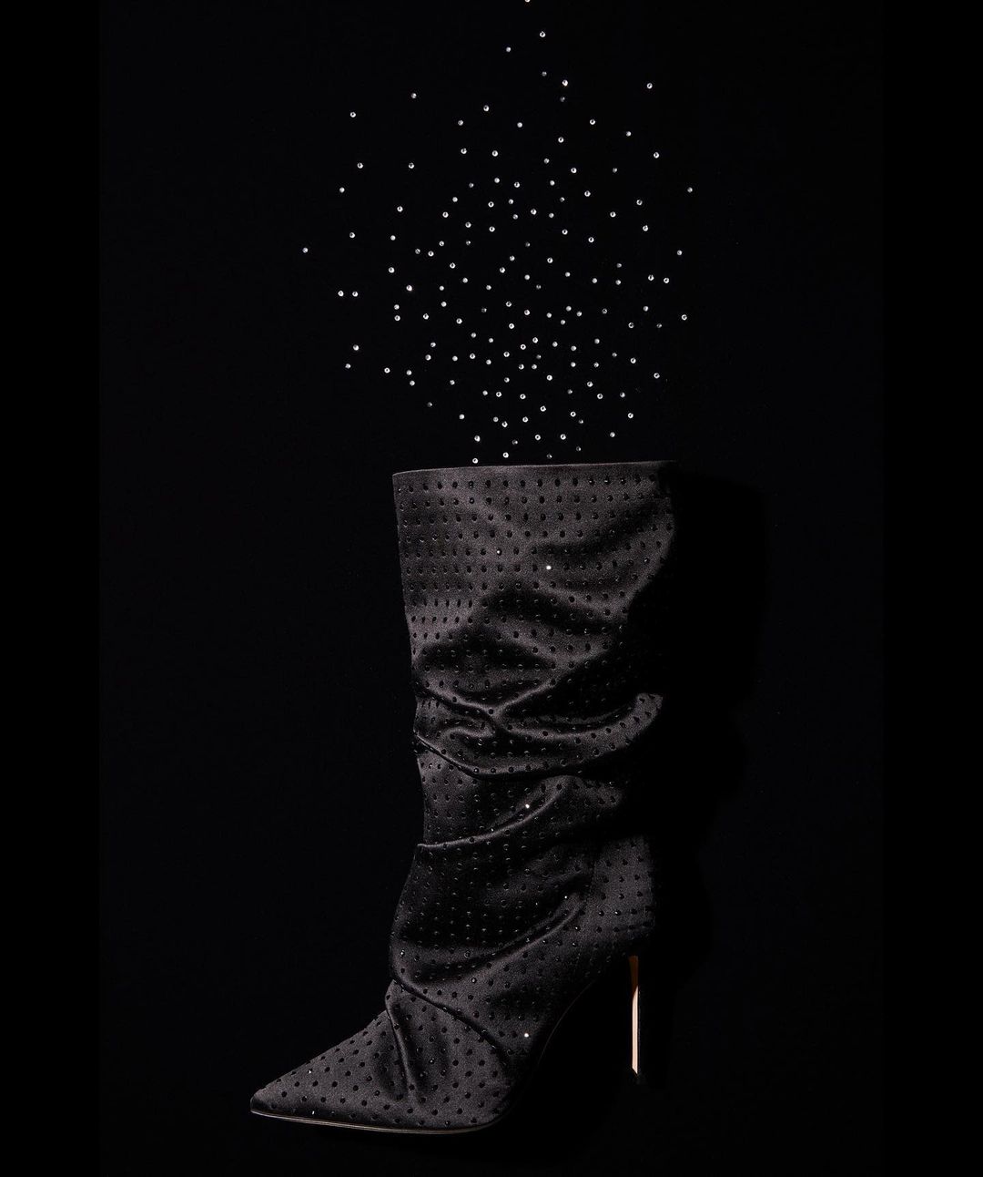 A black, over-the-knee, high-heeled boot is featured against a dark background, adorned with scattered dots or studs, evoking a celestial theme.
