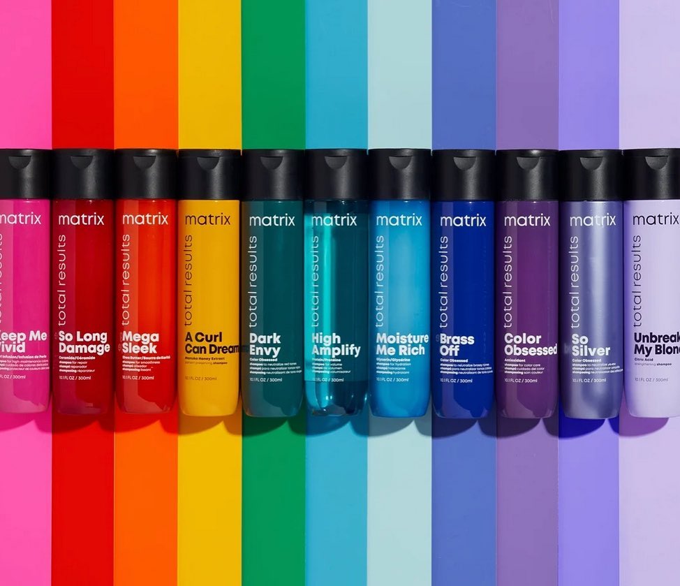 A row of vibrant Matrix Total Results hair product bottles displayed against a spectrum of matching colored backgrounds, product photography.